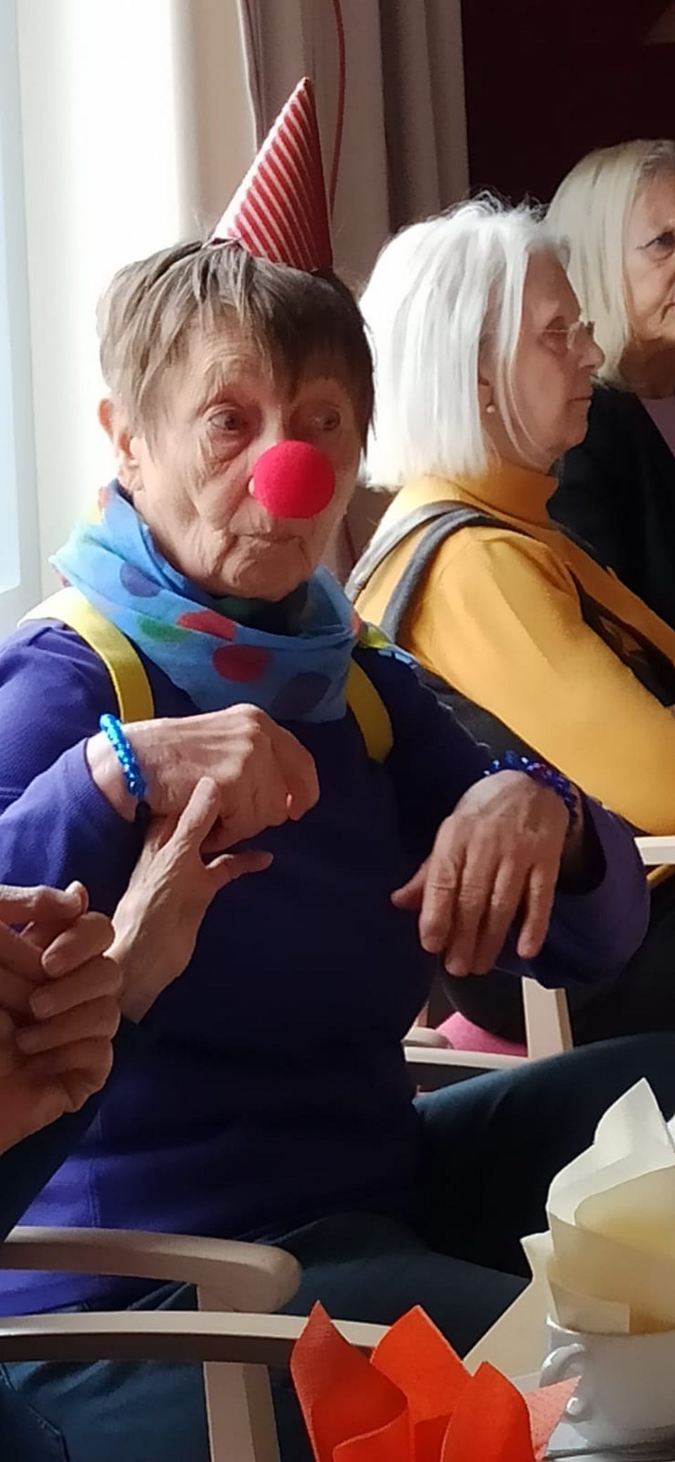 Eine ältere Dame trägt eine Karnevalsverkleidung mit roter Clowns-Nase und Spitzenhut.