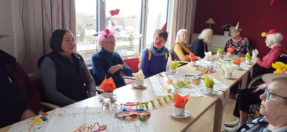 Zehn u.a. mit Hüten verkleidete Senior*innen sitzen an einer bunt geschmückten Kaffeetafel.