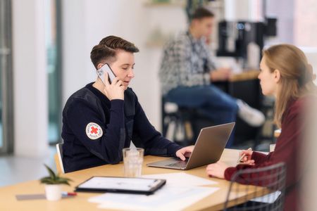 Mitarbeiterin des DRK arbeitet am Laptop und telefoniert mit einem Smartphone
