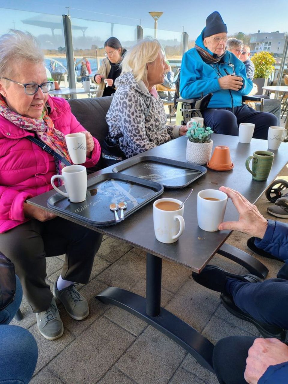 Eine Gruppe Senior*innen sitzt in einem Café um Tisch herum, auf dem einige Tassen stehen.