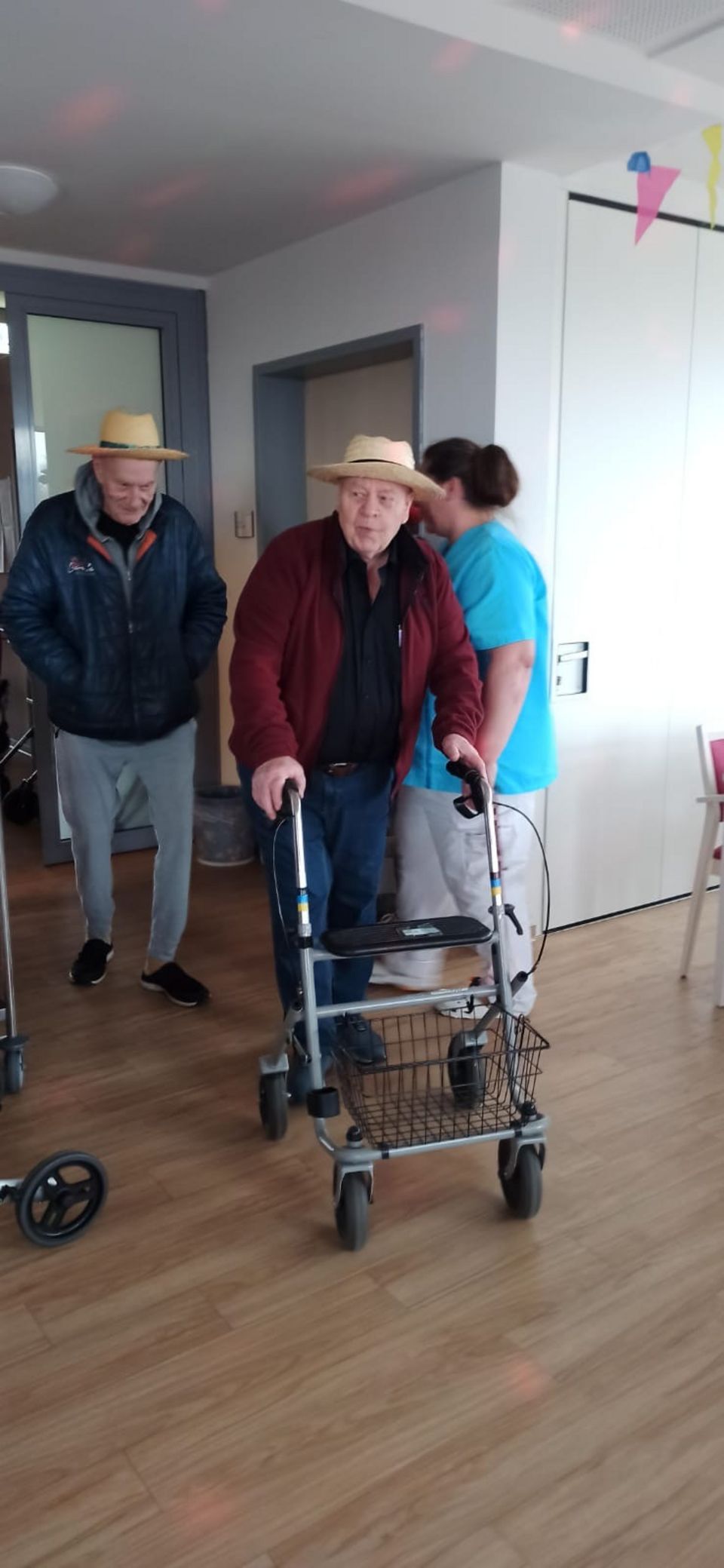 Zwei Senioren mit Strohhut betreten einen Veranstaltungssaal.