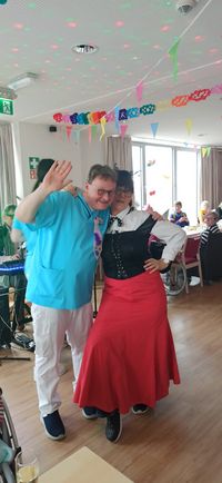 Ein Mann mit Jecken-Hut hält eine Rede in einem geschmückten Saal, in dem zahlreiche Senior*innen sitzen.